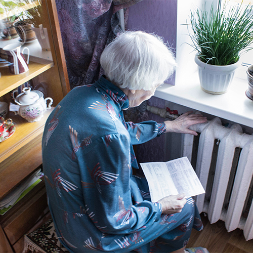 Illustrasjonsfoto av eldre dame med regning i hånden foran kald radiator. Foto: iStock.