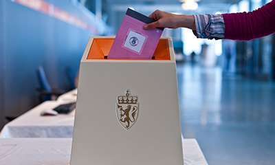 Hand som legg ein stemmeseddel i ei stemmeurne. Foto: Stortinget