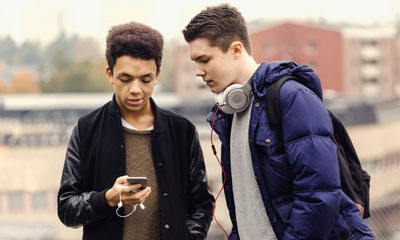To gutter som står sammen og ser på en mobiltelefon. Foto: Maskot/NTB7Scanpix