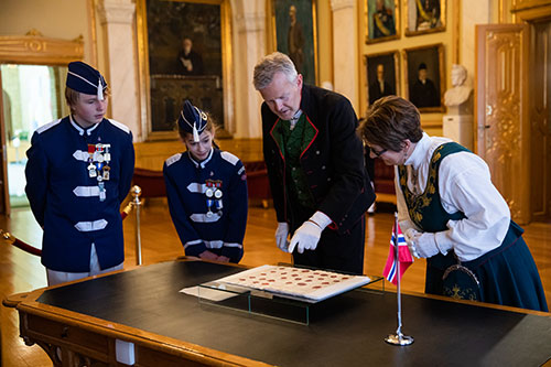 Stortingets arkivar Egil Borlaug og stortingspresident Tone Wilhelmsen Trøen ser på Grunnloven som ligger utstilt i Eidsvollsgalleriet sammen med skoleelevene Elinor Brørby Placucci og Magnus Slagsvold fra Vålerenga skole på 17. mai 2020. Foto: Stortinget.