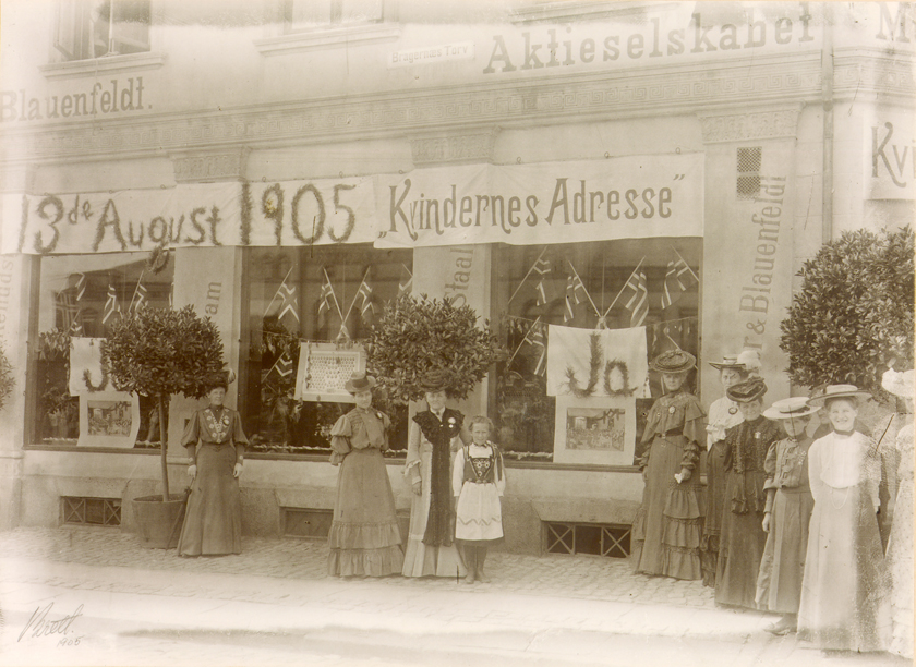 Foto av butikkfront i Drammen, med bannere til støtte for kvinnestemmerett.