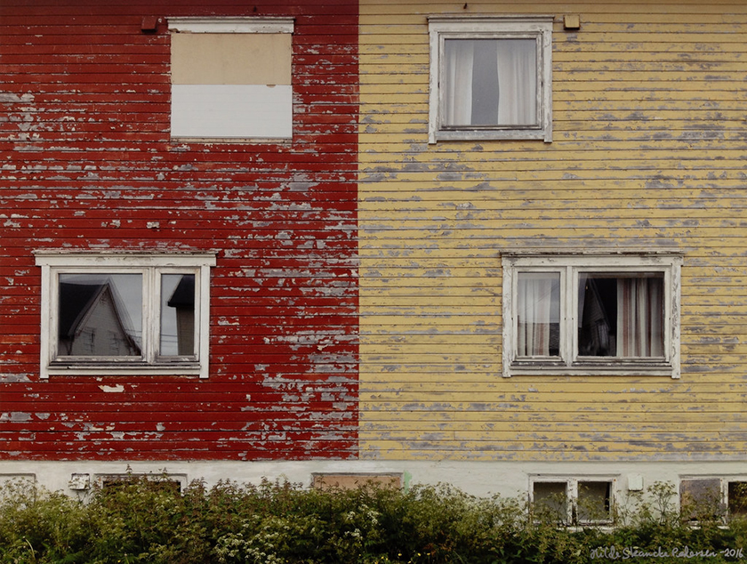 Fotografi av hus, malt i rødt og gult. Malingen er slitt av.